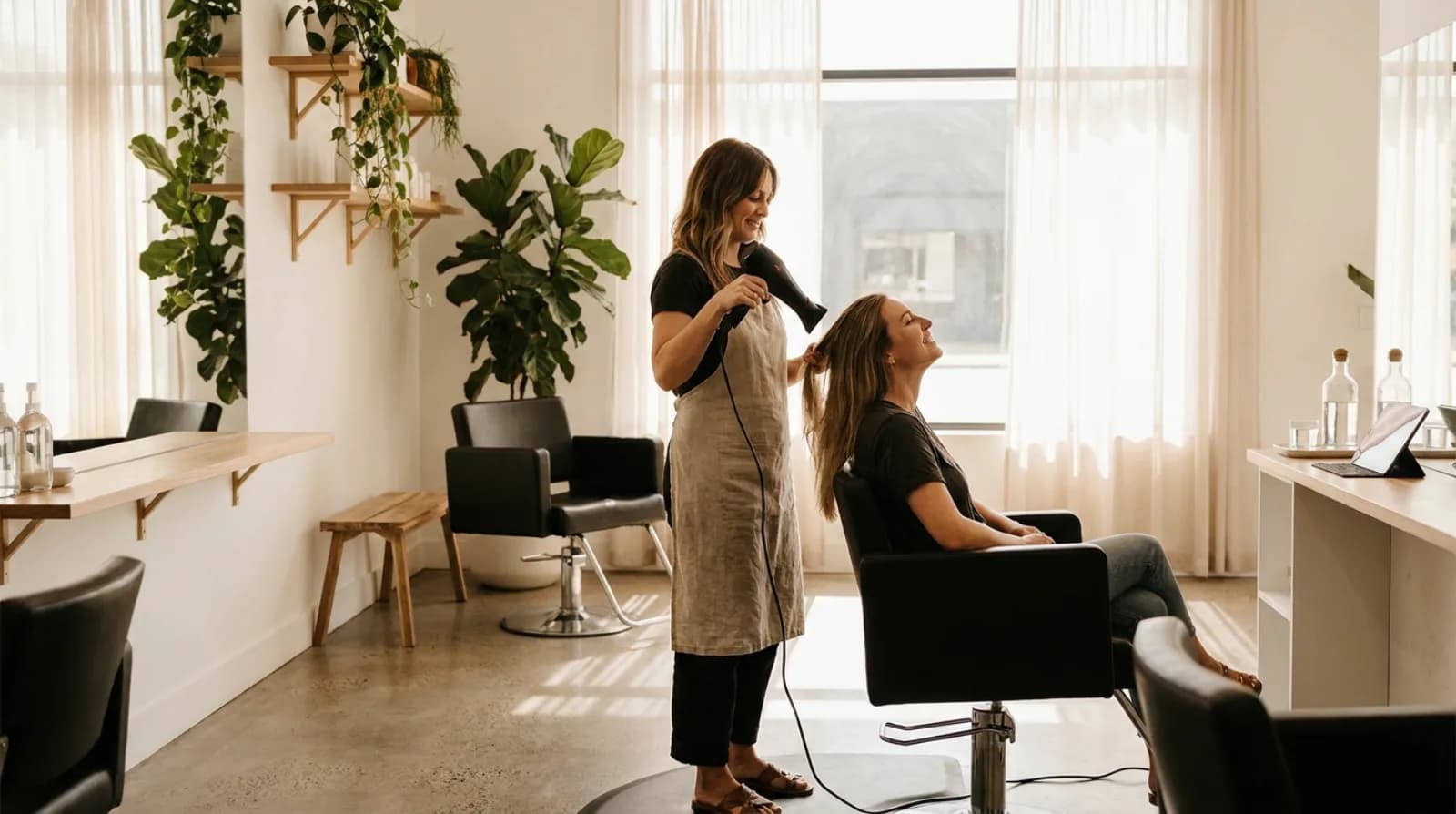 Stylist blow-drying a client's hair in a bright modern hair salon