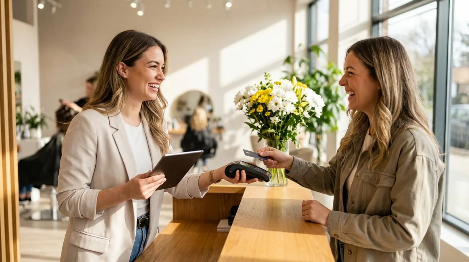 Salon receptionist taking a card payment from a smiling client at the front desk